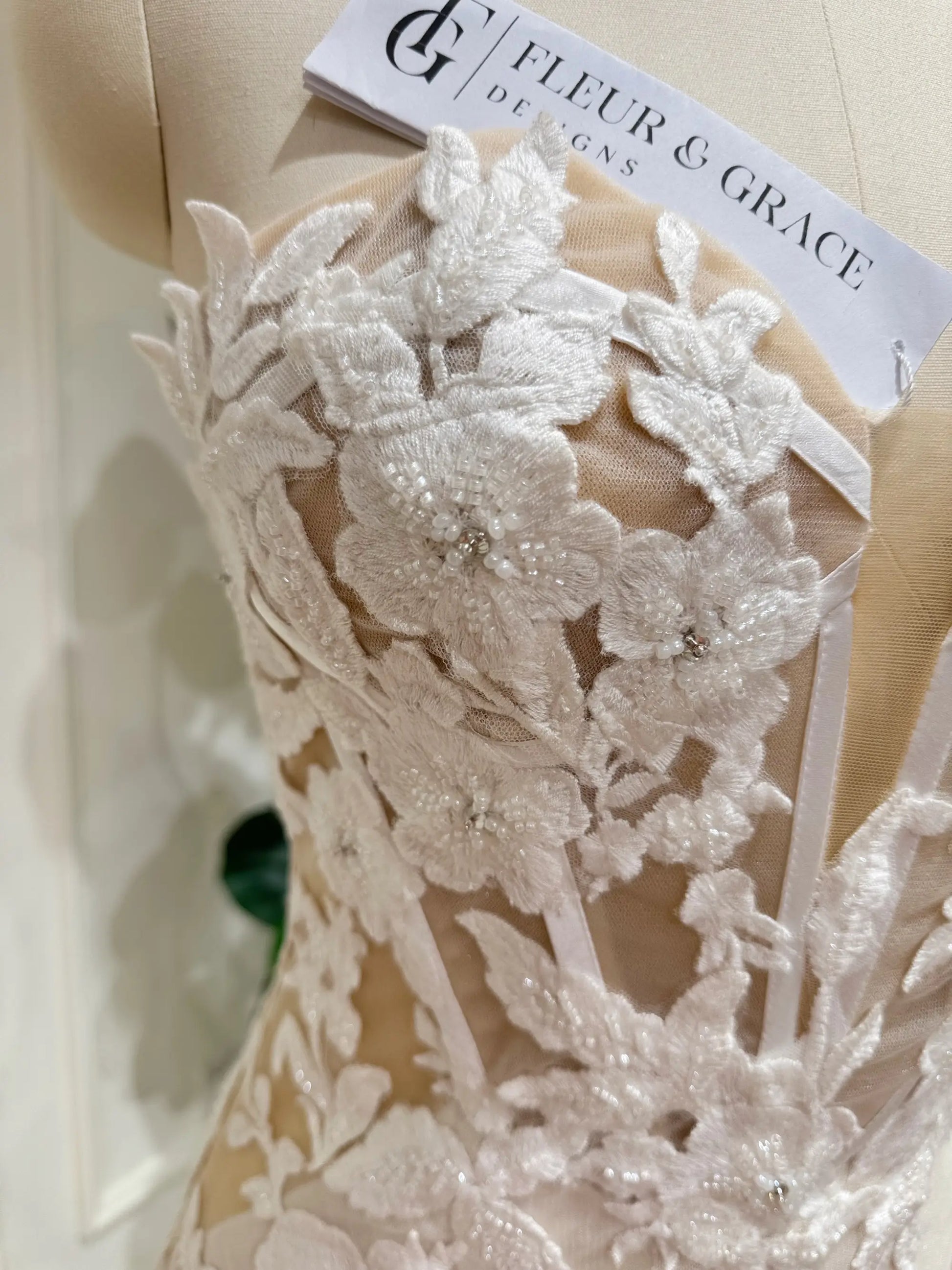 Tia Gown  by Fleur&Grace Designs — strapless mermaid wedding dress with basque waistline, sheer boned bodice, beige silk lining, ivory floral embroidery with beading, plunging V-neck, and court train.