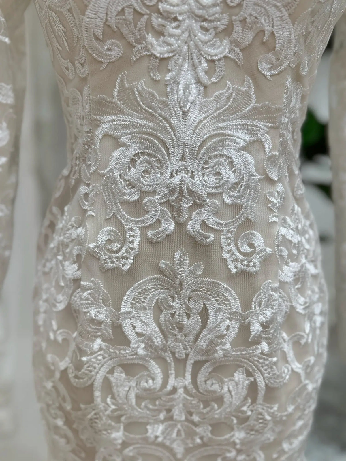 Close-up of intricate white beaded lace embroidery over nude illusion lining on a mermaid wedding dress.
