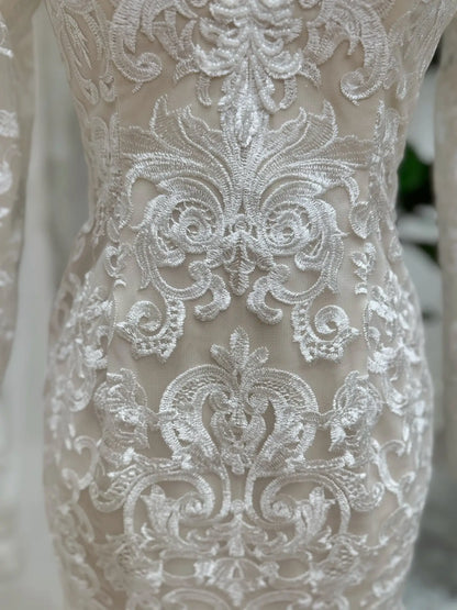Close-up of intricate white beaded lace embroidery over nude illusion lining on a mermaid wedding dress.