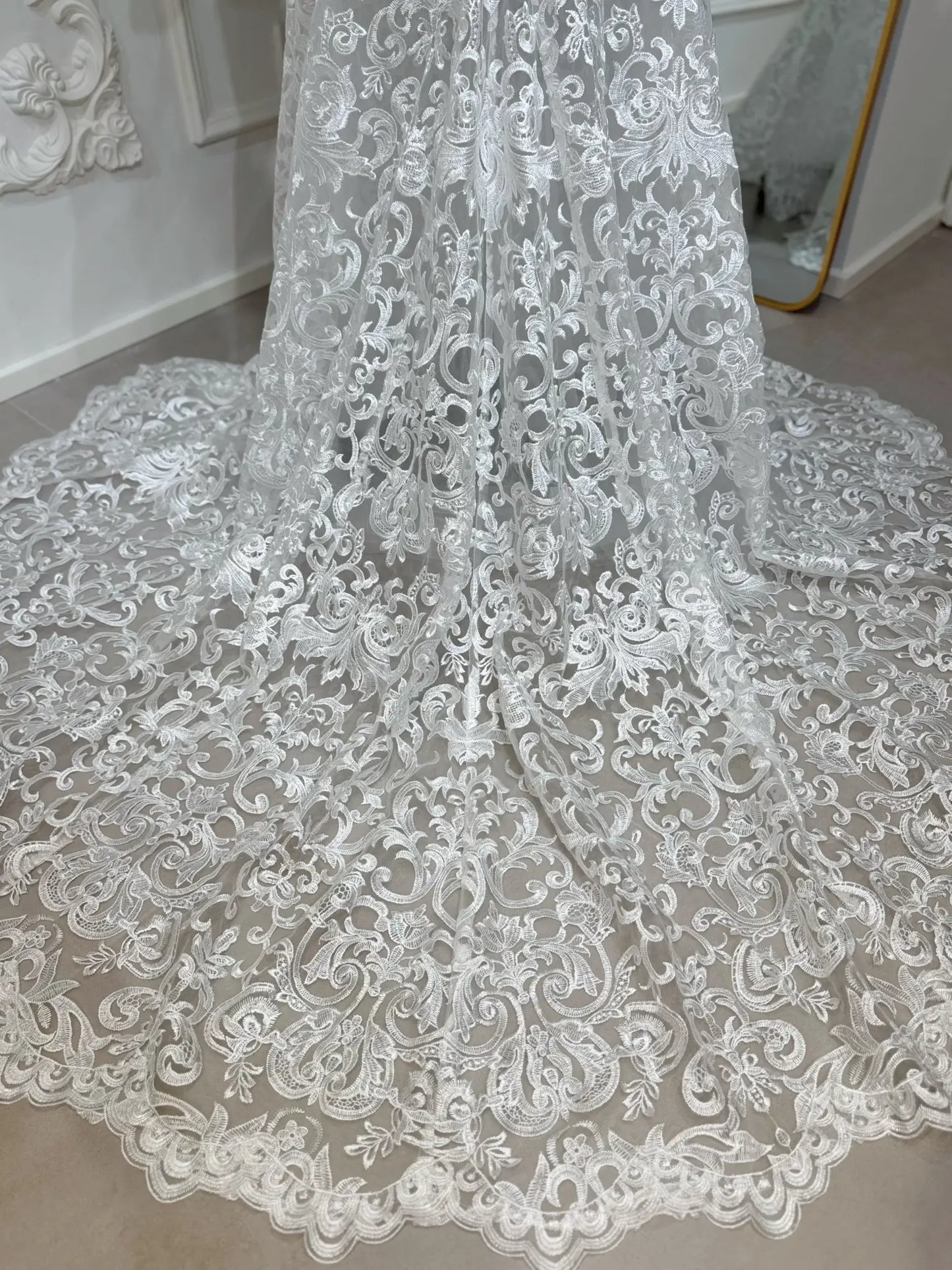 Intricate white beaded lace mermaid wedding dress train with scrolling floral motifs and a scalloped hem.