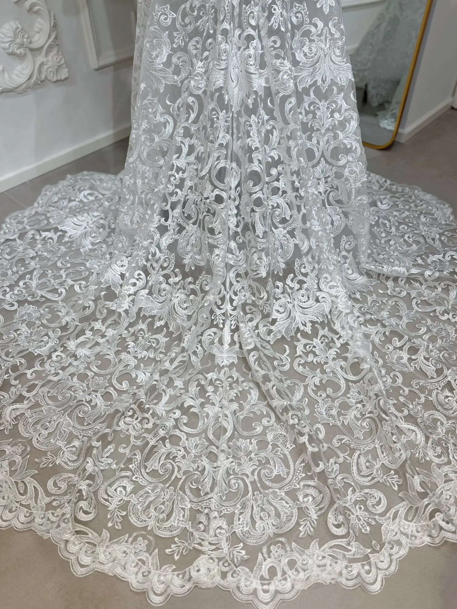 Intricate white beaded lace mermaid wedding dress train with scrolling floral motifs and a scalloped hem.