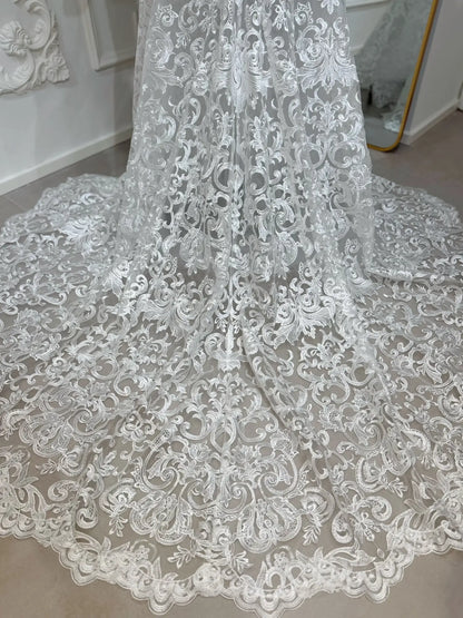 Intricate white beaded lace mermaid wedding dress train with scrolling floral motifs and a scalloped hem.