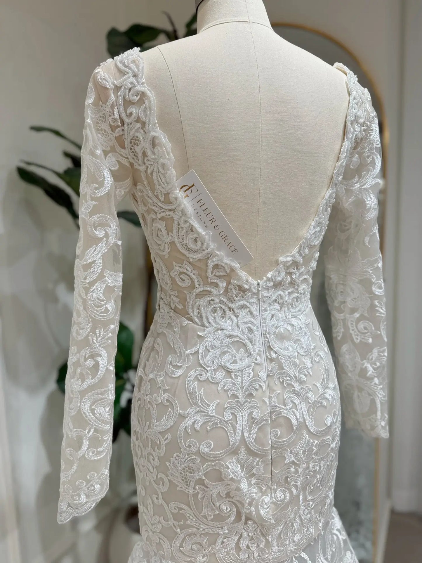 Beaded lace mermaid wedding dress with long sleeves and an elegant deep V-back on a mannequin.