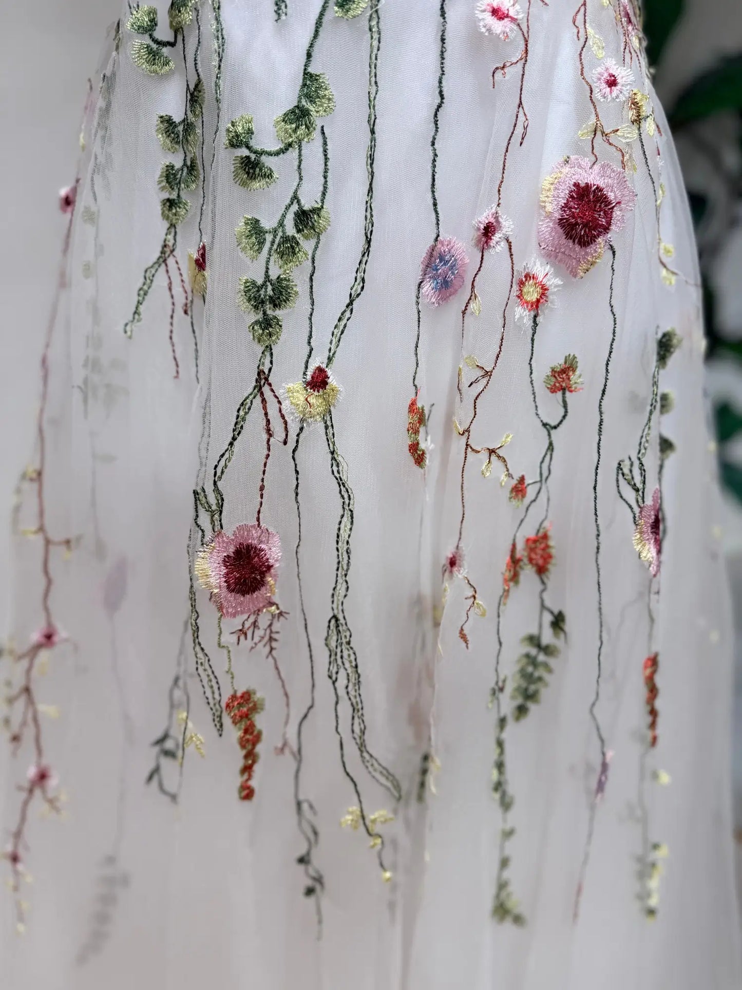 Soft tulle wedding dress featuring delicate pink, coral, and sage green botanical embroidery on a flowing A-line skirt.