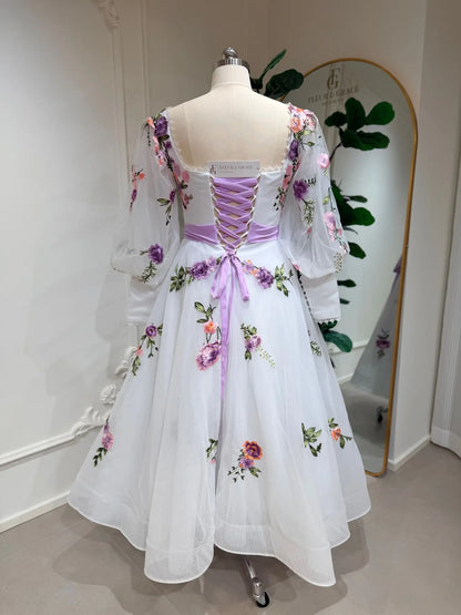 Tea-length wedding dress with lavender floral embroidery, puff sleeves, and a lavender lace-up corset back on a mannequin.