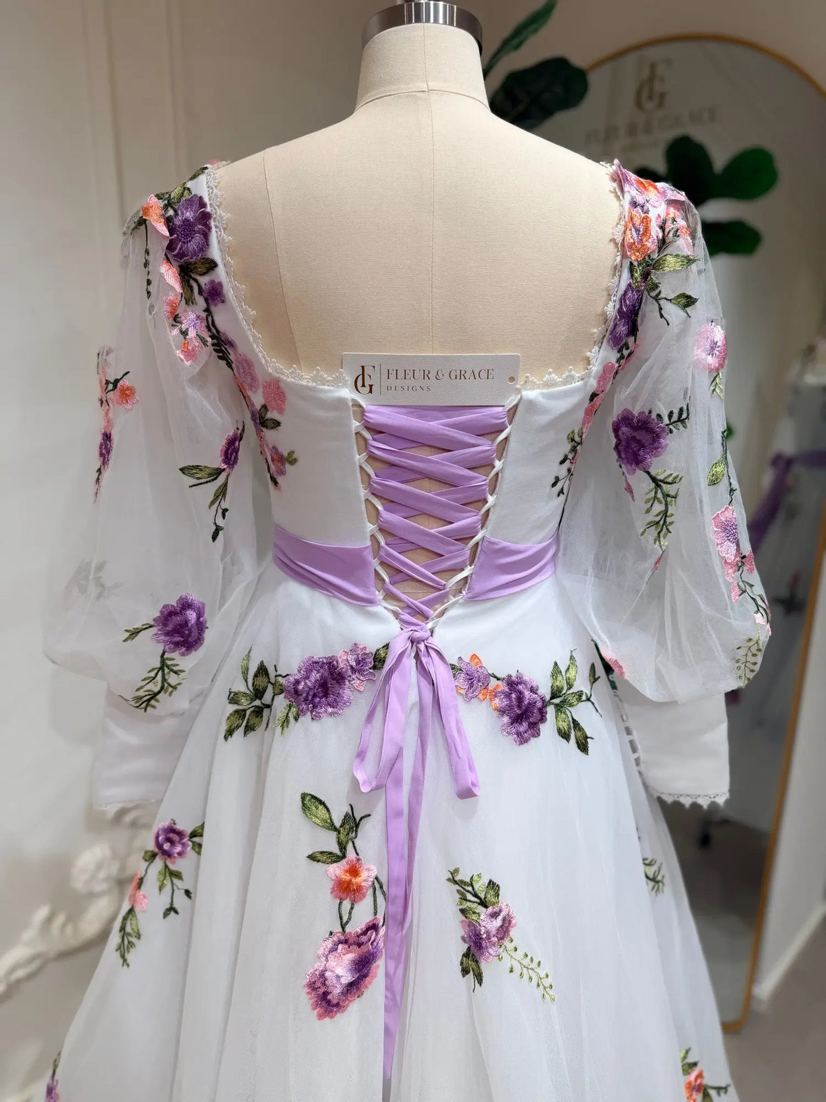 Tea-length wedding dress with lavender floral embroidery, puff sleeves, and a lavender lace-up corset back.