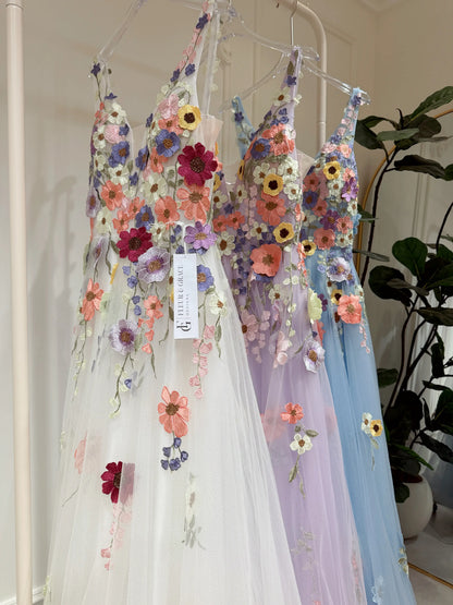 White, lavender, and blue A-line gowns featuring colorful wildflower embroidery, V-necklines, and sparkly mesh overlays.