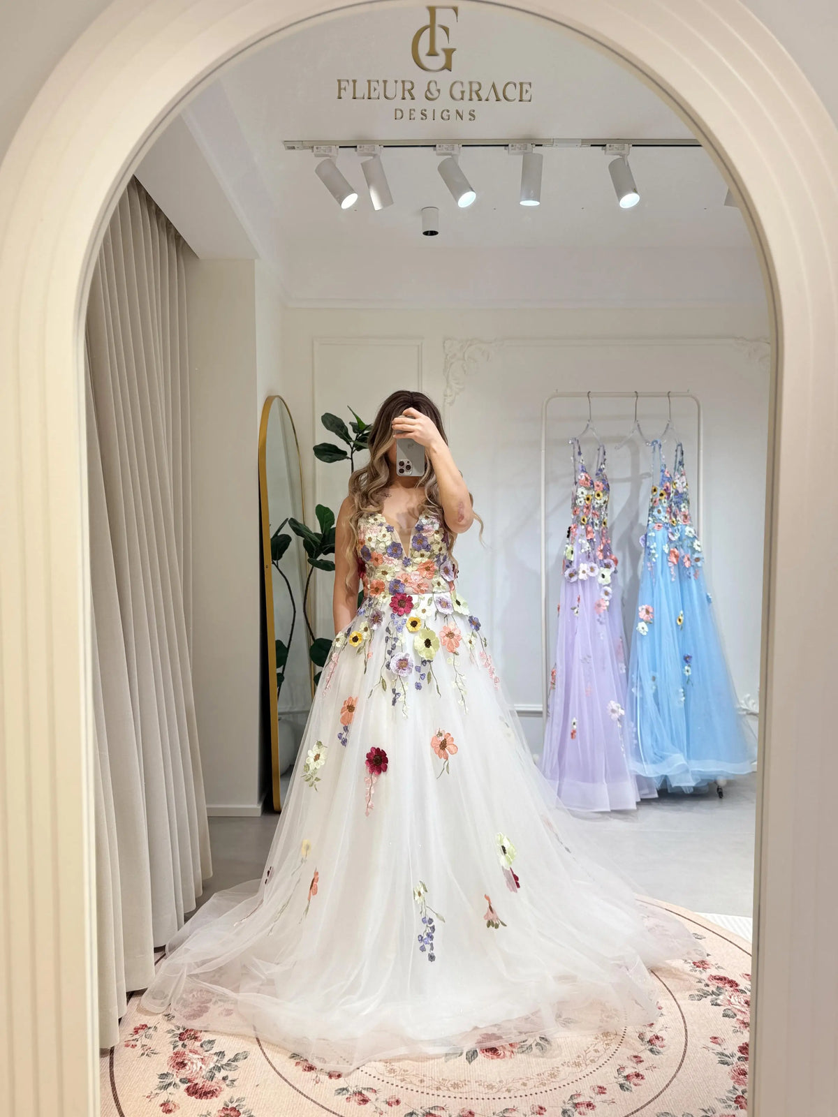White A-line gown with colorful wildflower embroidery, V-neckline, sparkly mesh overlay, and pockets in a bridal boutique.