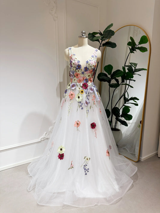 White A-line wedding gown with colorful wildflower embroidery, V-neckline, and sparkly mesh overlay on a mannequin.
