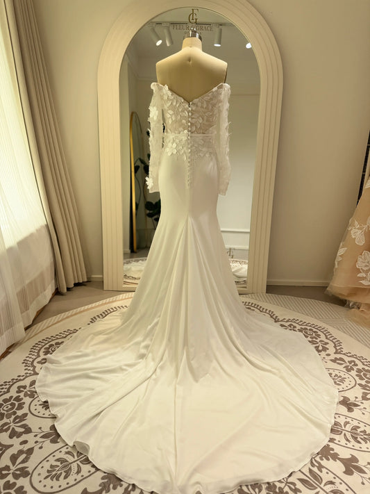 White crepe mermaid wedding gown with off-the-shoulder long sleeves and a sheer 3D floral appliqué bodice.