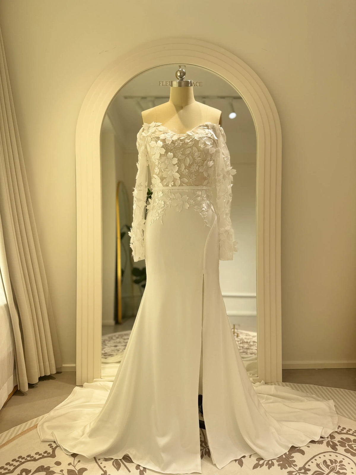 Minimalist white crepe mermaid wedding dress with 3D floral bodice, off-the-shoulder long sleeves, and a side slit.