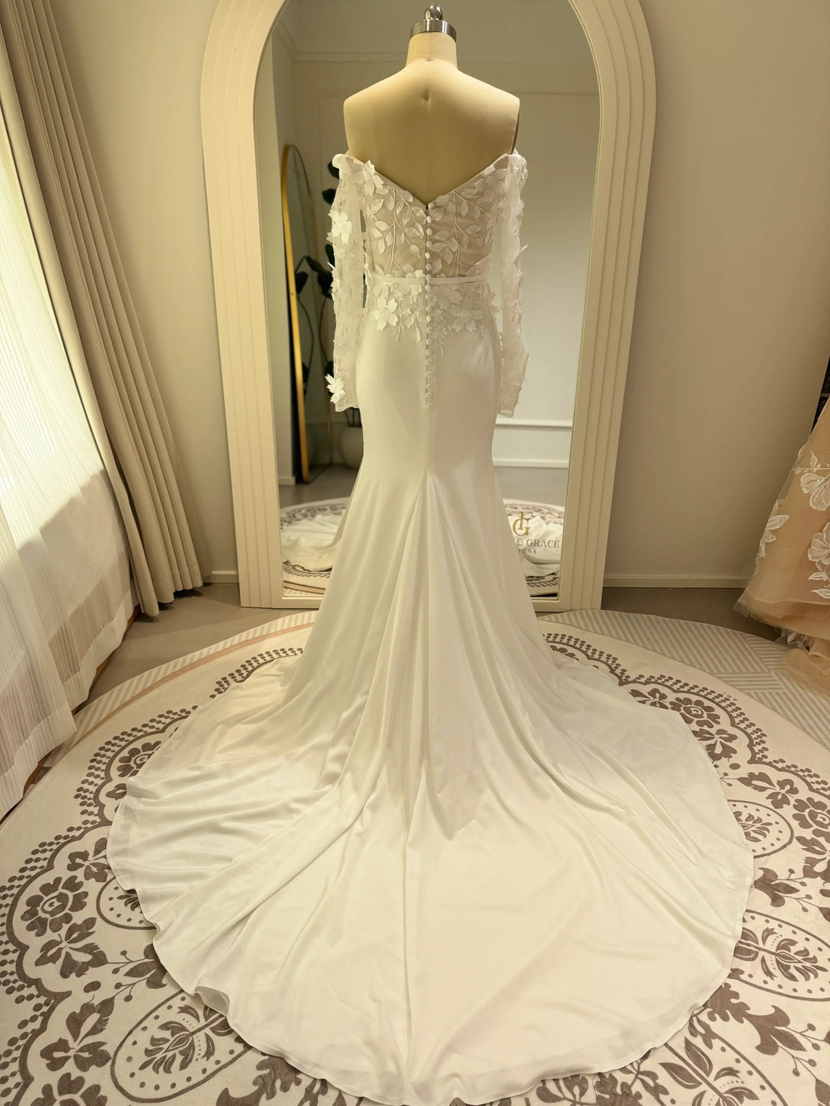 White mermaid wedding gown with 3D floral bodice, sheer off-the-shoulder long sleeves, and a flowing crepe train.