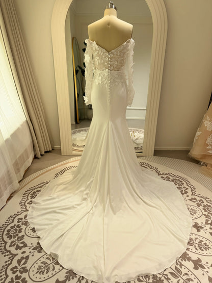 White mermaid wedding gown with 3D floral bodice, sheer off-the-shoulder long sleeves, and a flowing crepe train.