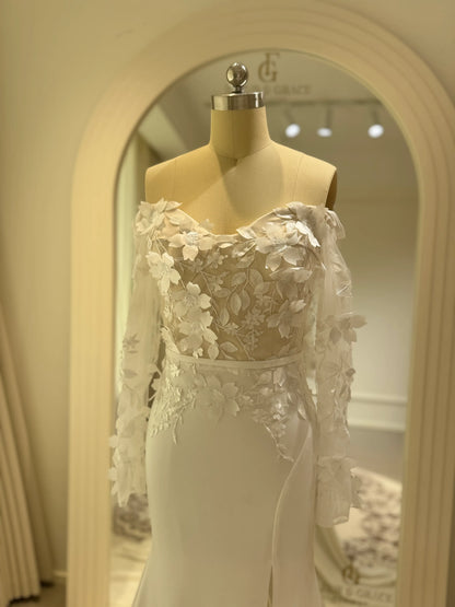 White crepe mermaid wedding gown with off-the-shoulder long sleeves and a 3D floral appliqué illusion bodice.