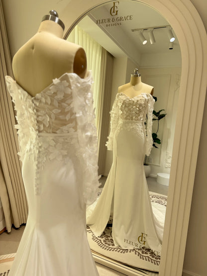 Minimalist white crepe mermaid wedding dress with 3D floral bodice, off-the-shoulder long sleeves, and side slit.