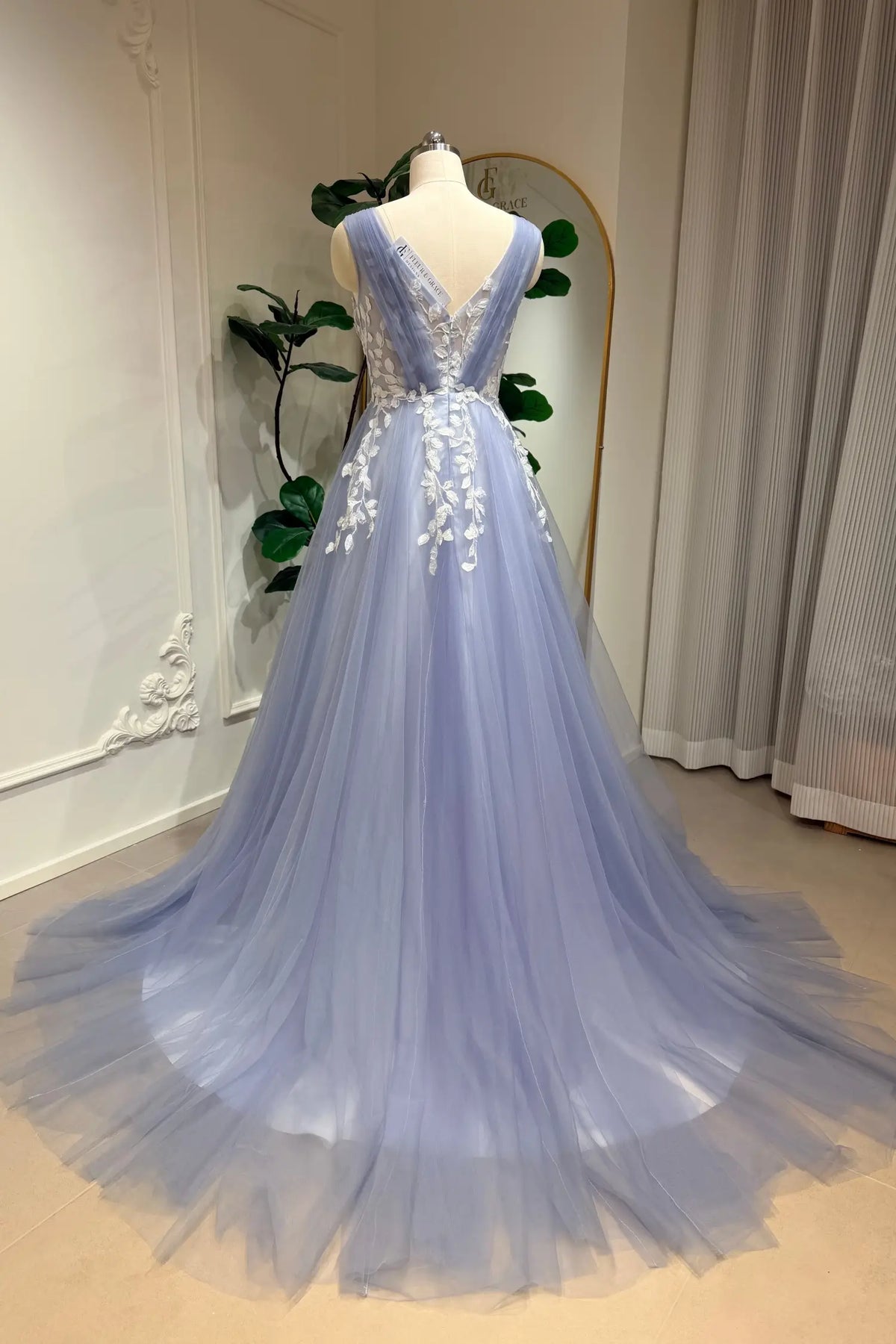 Dusty blue A-line wedding gown with a V-neck, tulle skirt, and intricate white floral lace appliqué on a mannequin.