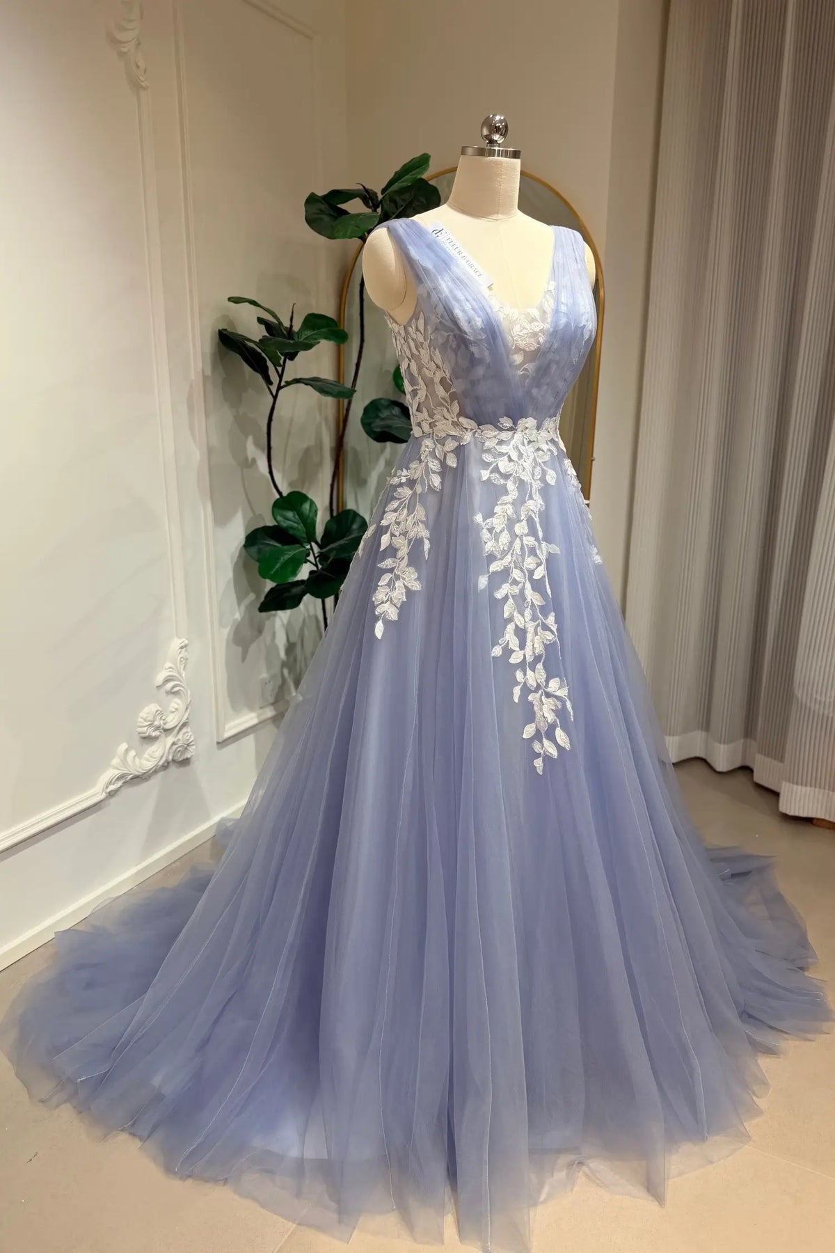 Dusty blue A-line wedding gown with a V-neck, tulle skirt, and intricate white floral lace appliqué on a mannequin.