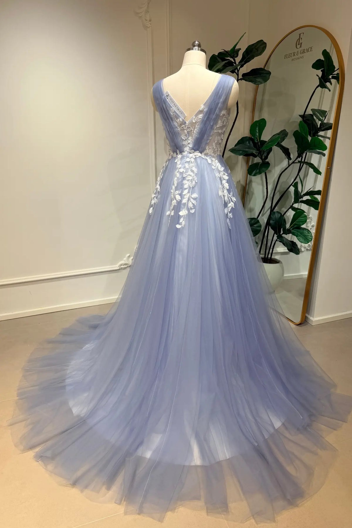 Dusty blue A-line wedding gown in tulle with a deep V-neck and intricate white floral lace appliqué on a mannequin.