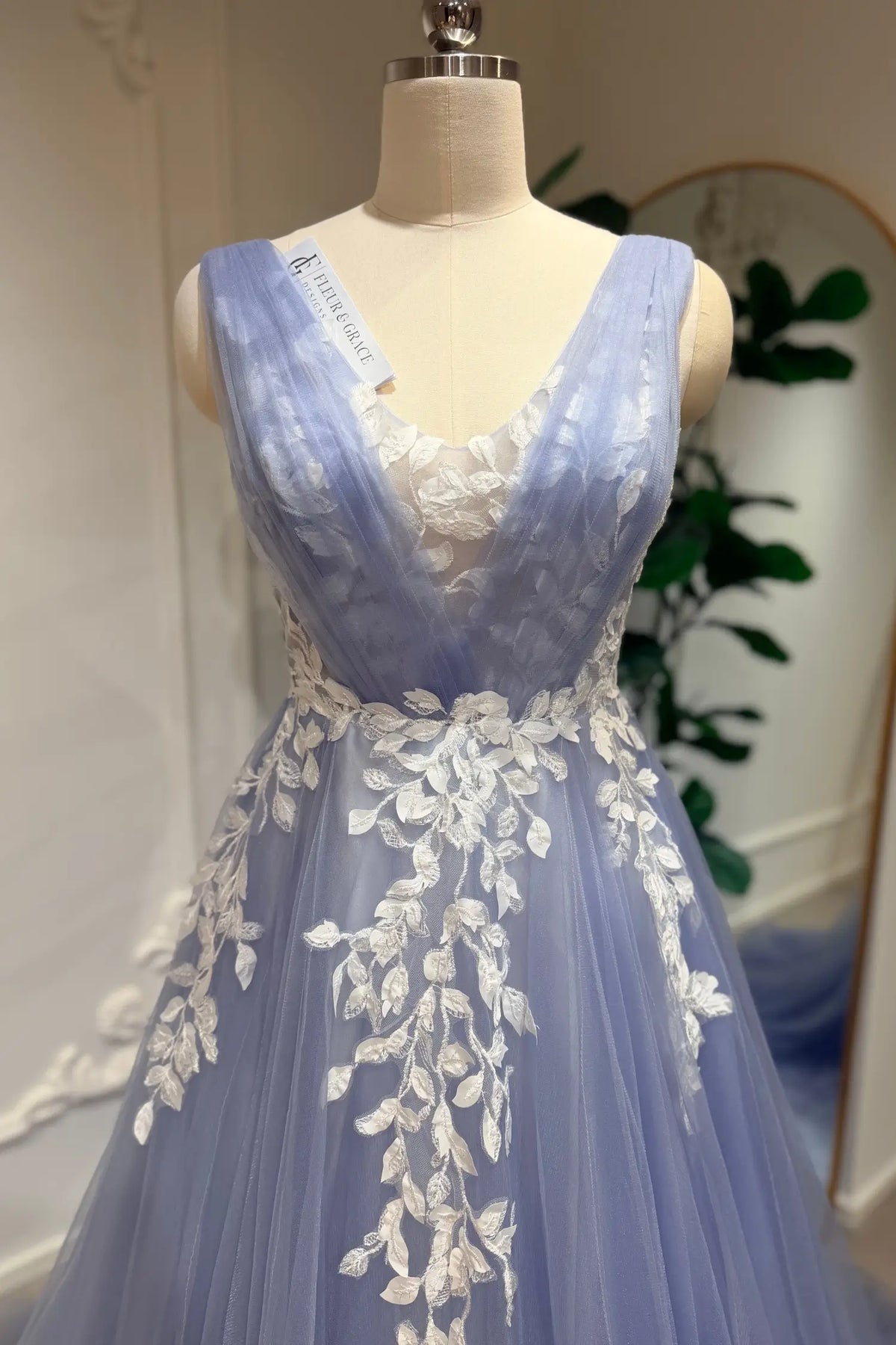 Dusty blue A-line wedding dress with a plunging V-neck, layered tulle, and intricate white floral lace appliqué.