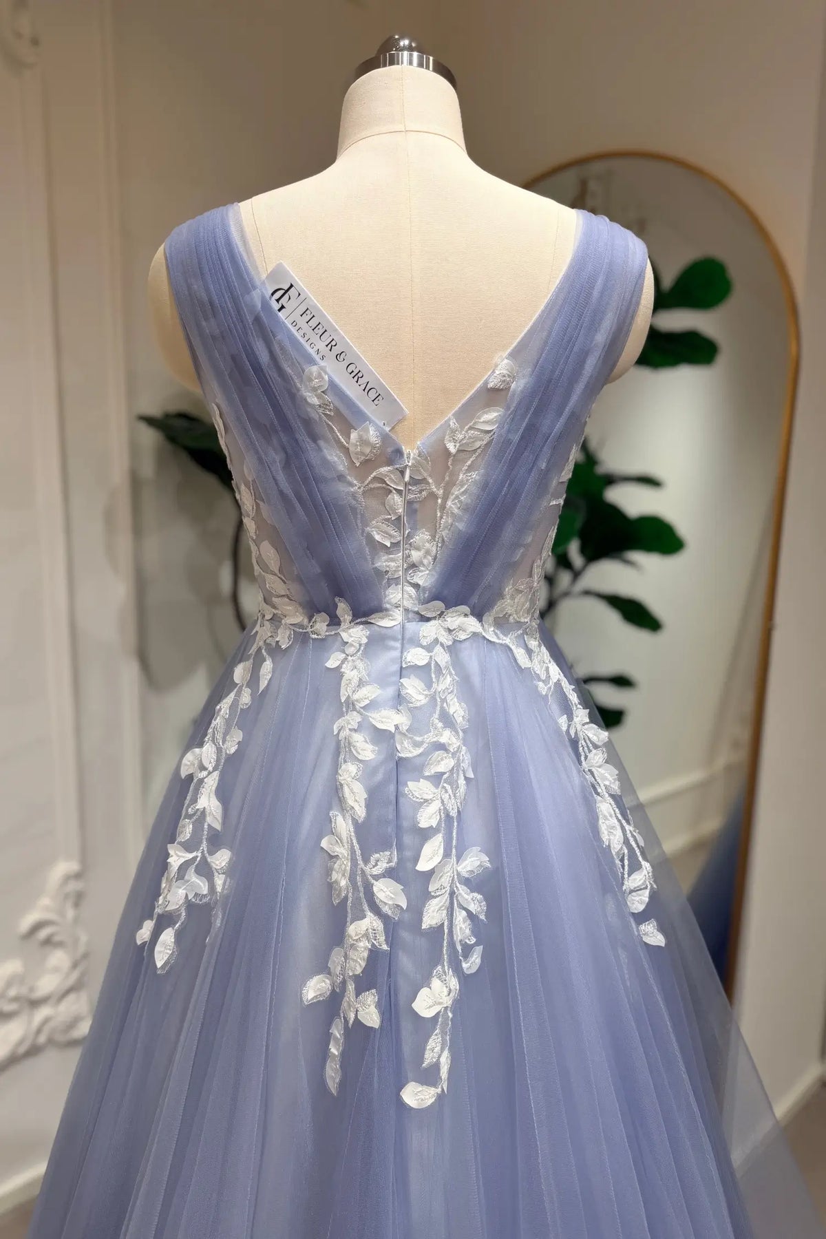 Dusty blue A-line wedding gown with white floral lace appliqué on layered tulle and a deep V-back design.