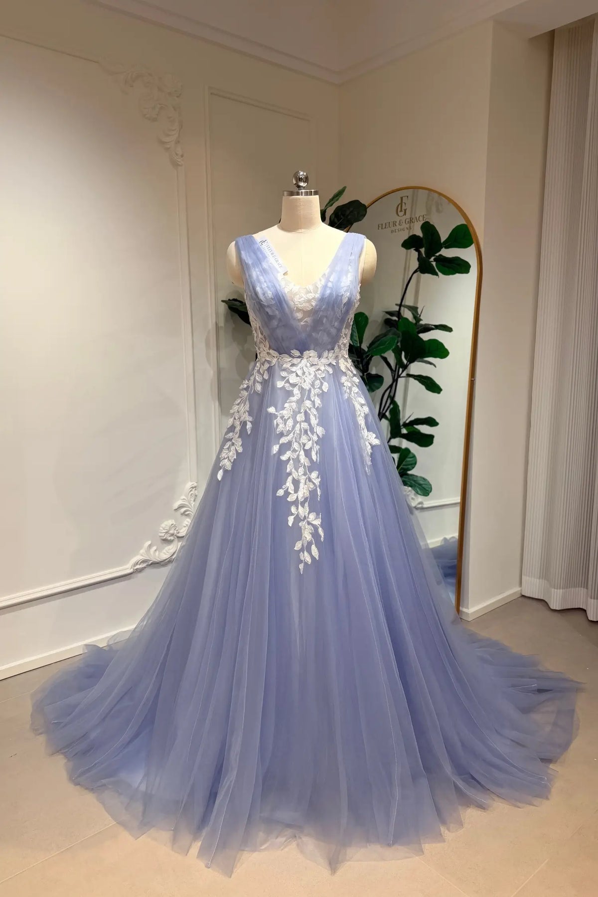 Dusty blue A-line wedding gown in tulle with a deep V-neck and intricate white floral lace appliqué on the bodice.