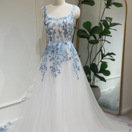 The Iris Gown by Fleur&Grace Designs is a graceful and romantic wedding dress adorned with elegant dusty blue floral embroidery. Crafted in soft tulle with a structured silhouette, this gown features a timeless square neckline, a comfortable built-in bodice, and pockets for modern functionality.