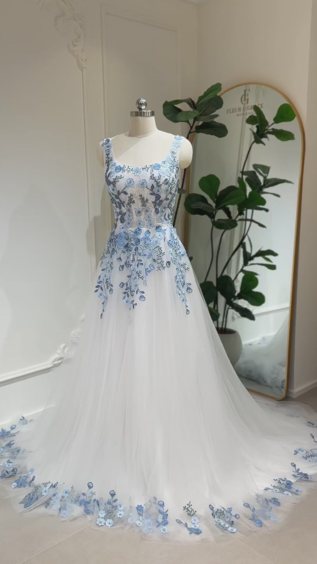 The Iris Gown by Fleur&Grace Designs is a graceful and romantic wedding dress adorned with elegant dusty blue floral embroidery. Crafted in soft tulle with a structured silhouette, this gown features a timeless square neckline, a comfortable built-in bodice, and pockets for modern functionality.