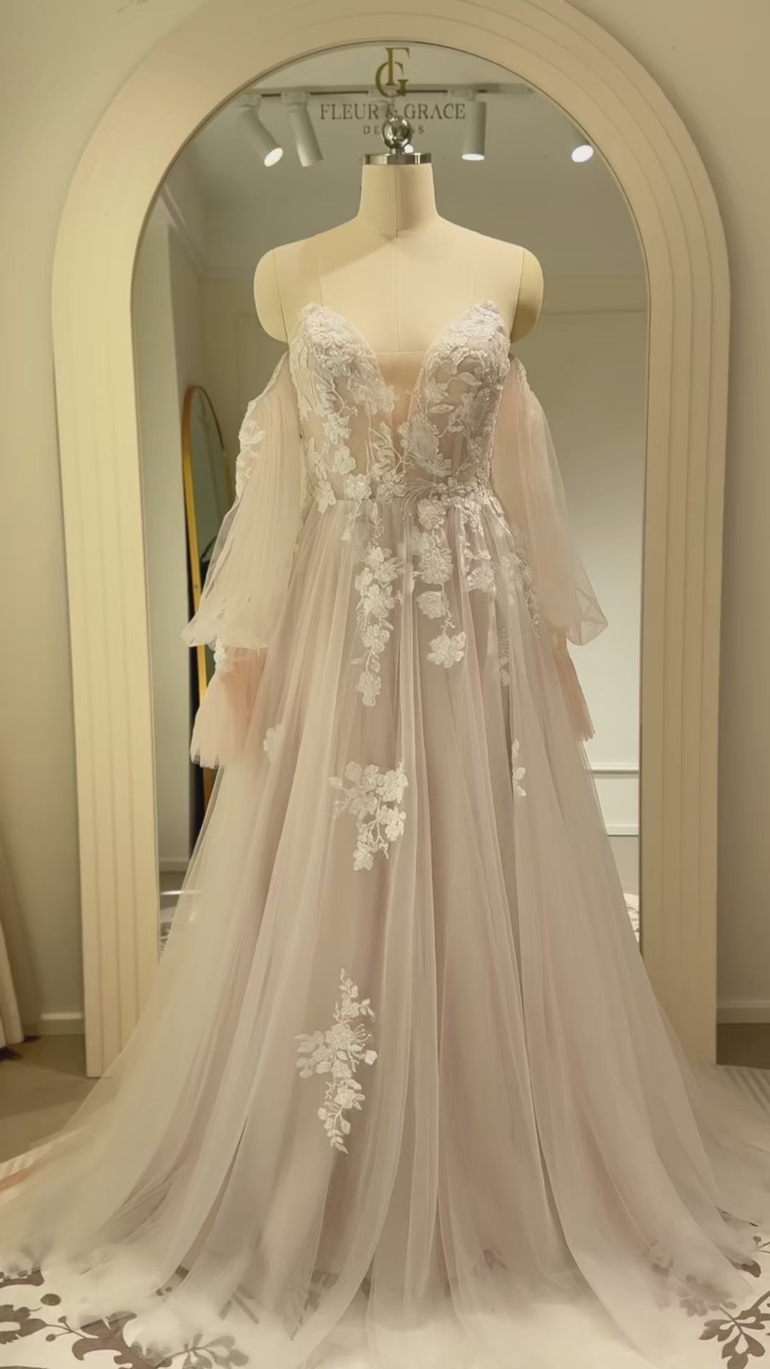 Aure Gown by Fleur&Grace Designs – romantic floral embroidered wedding dress with plunging neckline, removable long sleeves, soft tulle skirt, and A-line silhouette, perfect for whimsical weddings and elopements.