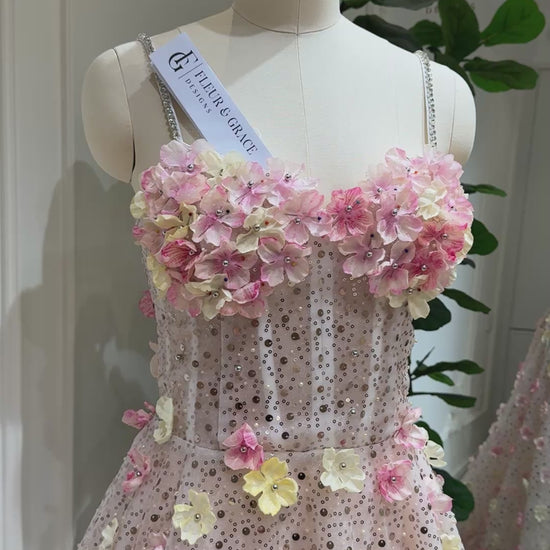 The Alice Gown FG018 is a dreamy, fairytale-inspired dress perfect for prom, photoshoots, and formal events. Crafted with exquisite beaded lace and adorned with delicate handmade 3D flowers in soft pink and yellow tones, this gown shimmers with every step. Featuring a romantic sweetheart neckline, lace‑up back for an adjustable fit, and thin stone‑accented straps, the Alice Gown blends fantasy with elegance. The regal court train adds a show‑stopping finish, making it ideal for prom nights, garden par