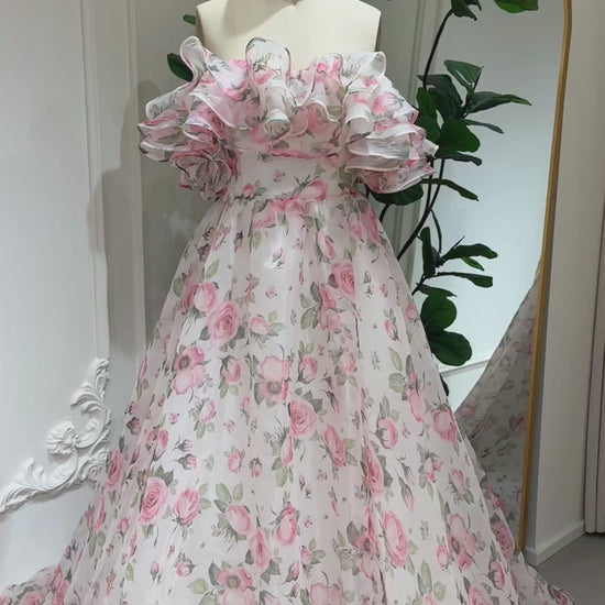 off‑the‑shoulder pink floral printed organza dress with tiered ruffle neckline, functional pockets, and flowing A‑line skirt, ideal for wedding photography and fairy‑tale events.-Model wearing the Rosie Gown FG026 by Fleur&Grace Designs 