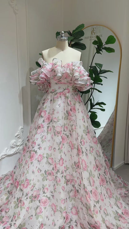 off‑the‑shoulder pink floral printed organza dress with tiered ruffle neckline, functional pockets, and flowing A‑line skirt, ideal for wedding photography and fairy‑tale events.-Model wearing the Rosie Gown FG026 by Fleur&Grace Designs 